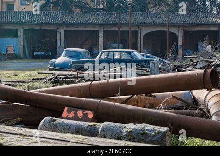 Große Rosty Pfeifen und alte Rosty Autos verlassen in einem Feld und zerbröckelt Lager im Hintergrund. Stockfoto