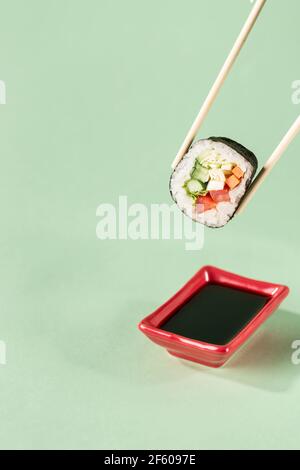 Brötchen mit frischem Gemüse mit Essstäbchen mit einem Teller für Sojasauce auf hellgrünem Hintergrund, Seitenansicht mit einer Textkopie. Veganes Sushi Stockfoto