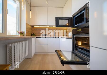 Moderne weiße und beige Holzküche mit Backofen geöffnet Stockfoto