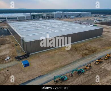 26. März 2021, Brandenburg, Grünheide: Die Baustelle des Tesla Gigafactory östlich von Berlin mit der Produktionshalle (Rückseite) und der Lackierhalle (Vorderseite, Luftaufnahme mit Drohne). Maximal 500.000 Fahrzeuge pro Jahr sollen ab Juli 2021 im Werk von der Produktionslinie Rollen - wobei der Automobilhersteller so schnell wie möglich das Maximum erreichen will. Der US-amerikanische Elektroauto-Hersteller erwartet vorerst, in seinem geplanten ersten Werk in Europa bis zu 10.500 Mitarbeiter im Schichtbetrieb beschäftigen zu können. Foto: Patrick Pleul/dpa-Zentralbild/ZB Stockfoto