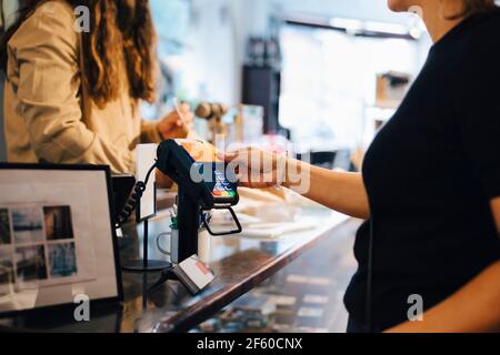 Zugeschnittenes Bild eines männlichen Kunden, der mit Kreditkarte bezahlt Weibliche Besitzerin im Einzelhandelsgeschäft Stockfoto