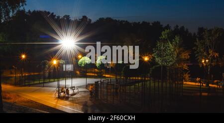 Grüne Nacht leerer Spielplatz im Park mit hellem Scheinwerfer auf blauem Hintergrund. Abend Stadt Stadtlandschaft. Niemand im Sommer öffentlichen Platz. Sport Stockfoto