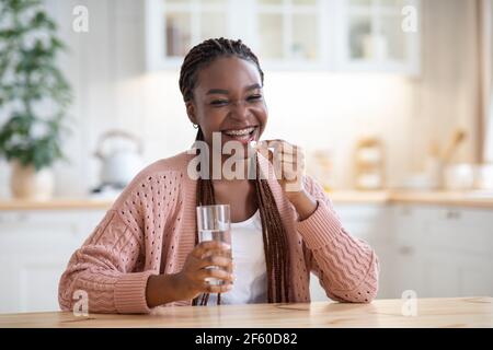Schönheitspflege. Positive Black Female Einnahme Von Vitamin-Pille Und Wasser Zu Hause Stockfoto