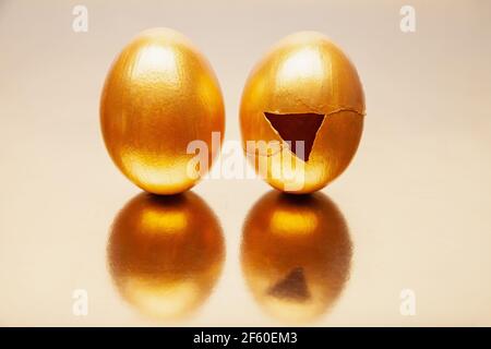 Ganze und geknackte goldene Eier auf reflektierenden Tisch gelegt Stockfoto