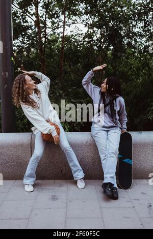 Weibliche Freunde machen High-Five, während sie an der Stützmauer sitzen Fußweg Stockfoto