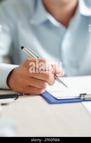 Nahaufnahme des Geschäftsmannes, der am Bürotisch sitzt und analysiert Liniendiagramm in der Zwischenablage Stockfoto