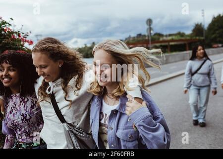 Lächelnde Freunde mit den Armen, die auf einem Fußweg gegen den Himmel laufen Stockfoto