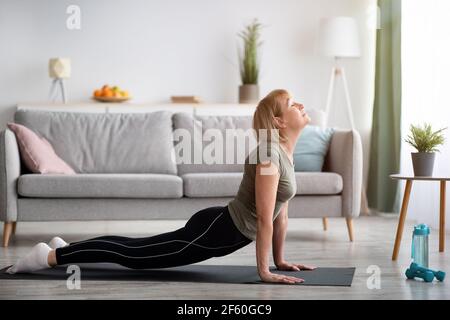 In voller Länge fit Senior Frau Kobra Pose auf Yoga-Matte im Wohnzimmer, leeren Raum Stockfoto
