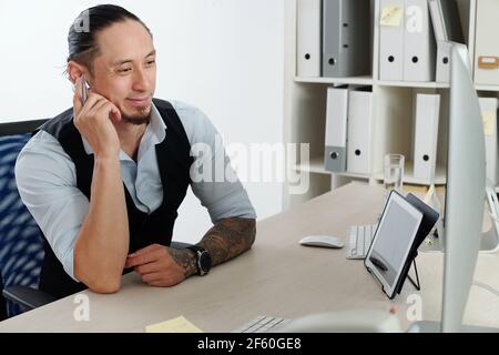 Glücklich lächelnde Händler in formalwear hören gute Nachrichten in Ohrhörer und Blick auf den Computerbildschirm Stockfoto