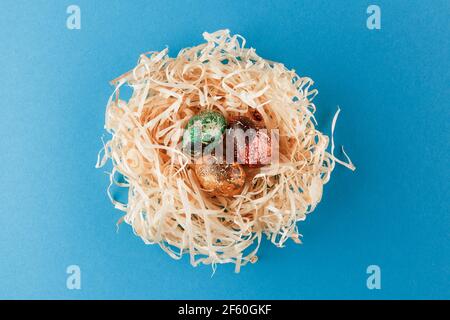 Drei ostereier sind rot, gelb und grün gefärbt. Eier liegen in einem Nest aus Holzspänen. Bemalte ostereier auf blauem Hintergrund. Flach liegend. Stockfoto