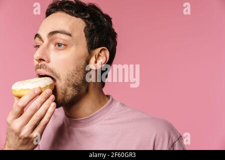 Zufrieden gut aussehend hungrig Kerl essen Donut auf Kamera isoliert über Rosa Hintergrund Stockfoto