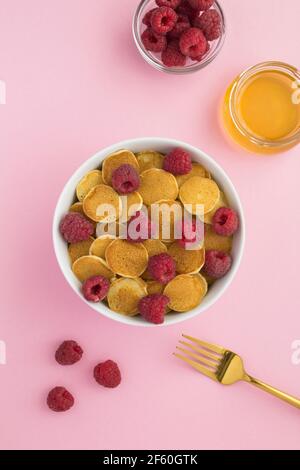 Draufsicht auf Mini-Pfannkuchen mit Himbeeren in weiß Schüssel auf der rosa Oberfläche Stockfoto
