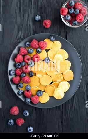 Draufsicht auf Mini-Pfannkuchen mit Beeren in schwarz Platte auf dem dunklen Hintergrund Stockfoto