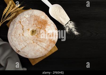 Hausgemachtes Weizenbrot auf dem braunen Schneidebrett auf dem schwarzen Holzhintergrund. Draufsicht. Speicherplatz kopieren. Stockfoto