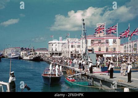 Crowd Scenes in Bridgetown, Barbados, 1955, während der Karibik-Tour von Prinzessin Margaret. Hier säumen Menschenmassen den Hafen am Trafalgar Square (heute National Heroes Square genannt). Hier kommt ein Tender der vertäuten Royal Yacht ‘Britannia’. Im Januar 1955 unternahm die Prinzessin ihre ersten Reisen in die Karibik, ihre Reise an Bord von Britannia in die britischen Kolonien war in ganz Westindien beliebt. Prinzessin Margaret (1930 – 2002) war die Schwester von Königin Elisabeth II. Dieses Bild stammt von einem alten Amateur-35-mm-Farbtransparenz – einem Vintage-Foto aus den 1950er Jahren. Stockfoto