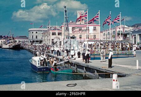 Crowd Scenes in Bridgetown, Barbados, 1955, während der Karibik-Tour von Prinzessin Margaret. Hier säumen Menschenmassen den Hafen am Trafalgar Square (heute National Heroes Square genannt). Würdenträger steigen an Bord der Tender, ‘Lynx’, um zur festgetäuten Royal Yacht ‘Britannia’ hinausgefahren zu werden. Im Januar 1955 machte die Prinzessin die erste von vielen Reisen in die Karibik, ihre Tour an Bord von Britannia zu den britischen Kolonien war in ganz Westindien beliebt. Prinzessin Margaret (1930 – 2002) war die Schwester von Königin Elisabeth II. Dieses Bild stammt von einem alten Amateur-35-mm-Farbtransparenz – einem Vintage-Foto aus den 1950er Jahren Stockfoto