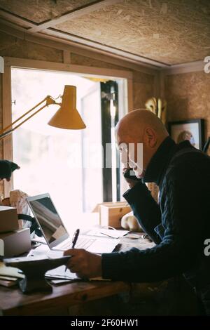 Geschäftsmann, der in der Werkstatt mit einem Laptop über ein Mobiltelefon spricht Stockfoto