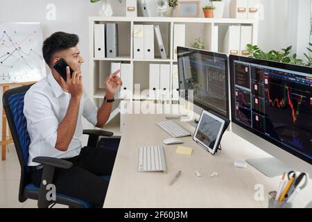 Positive indische Trader Analyse Aktiendaten auf Computerbildschirmen und Telefonische Beratung von Kunden Stockfoto