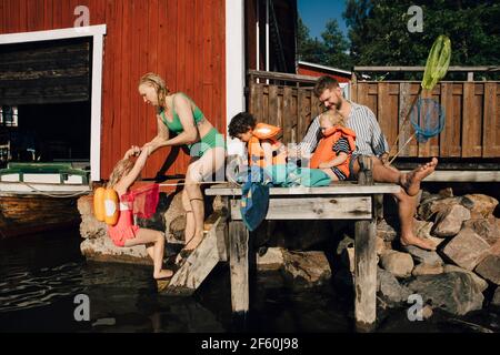 Vater mit Kindern, die während der Sommerferien auf dem Pier sitzen Stockfoto