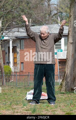 Ein asiatischer Amerikaner, der wahrscheinlich in den Achtzigern ist, führt eine kleine Gruppe in Tai Chi-Bewegungsübungen in einem Park in Queens, New York City.Vertical, Stockfoto