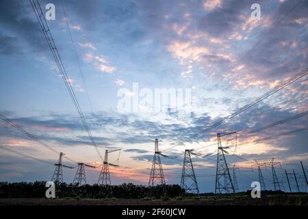 Elektrische Masten und Hochspannungsleitungen im Hintergrund bei Sonnenuntergang. Gruppieren Sie die Silhouette der Sendetürme. Stockfoto