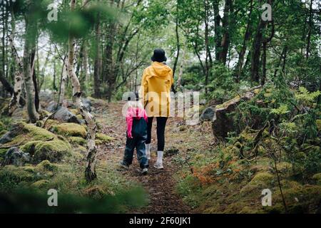 Rückansicht von Mutter und Tochter, die im Wald spazieren gehen Stockfoto