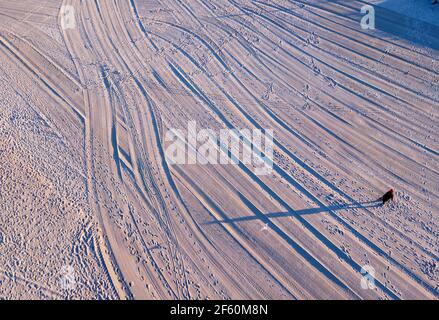 Ahlbeck, Deutschland. März 2021, 22nd. Ein Spaziergänger wirft einen langen Schatten auf den Strand, der von der untergehenden Sonne orange-rot beleuchtet wird. (Luftaufnahme mit Drohne) Quelle: Jens Büttner/dpa-Zentralbild/ZB/dpa/Alamy Live News Stockfoto