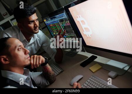 Nachdenkliche Trader diskutieren aufsteigende Bitcoin-Preisdiagramm auf dem Computerbildschirm Bei der Arbeit im dunklen Büro Stockfoto