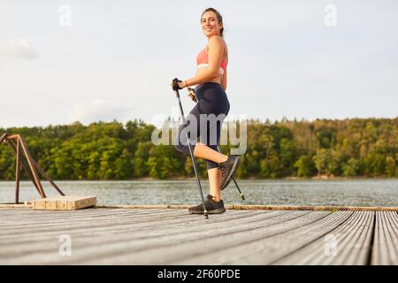 Junge Frau beim nordic Walking für Ausdauer und Fitness in Natur am See Stockfoto