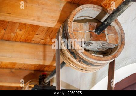 Altes Holzrad auf einem Schacht als Teil eines Getriebeantriebs unter den Deckenbalken einer alten Zimmermannsfabrik. Stockfoto