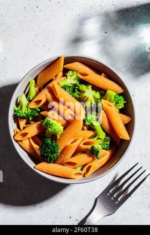 Rote Linsennudeln mit Brokkoli in einer grauen Schüssel. Gesunde vegane Pasta mit Gemüse. Stockfoto