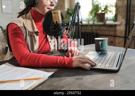 Nahaufnahme einer Frau in Kopfhörern, die am Tisch sitzt und Arbeiten am Laptop im Radiostudio Stockfoto