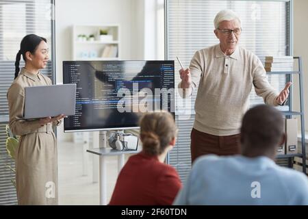 Portrait des modernen Senior Geschäftsmann geben Präsentation im Büro zu IT-Team mit Code auf dem Bildschirm, Kopierraum Stockfoto