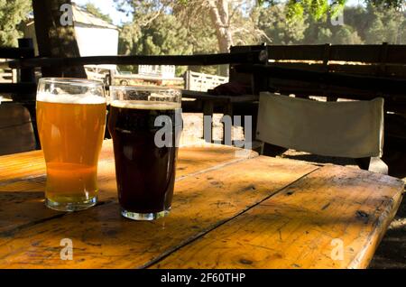 Zwei Gläser Bier, ein blondes Pint und ein schwarzes Pint, Craft Beer, in einem Biergarten im Freien, Stockfoto