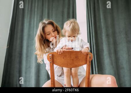 Glückliche junge Mutter sitzt auf einem Stuhl und hält ihren kleinen Sohn. Stockfoto