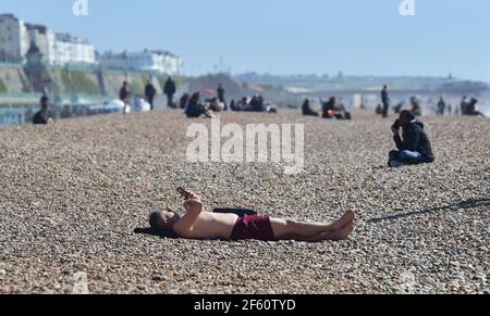 Brighton UK 29th March 2021 - EIN Sonnenanbeter genießt einen schönen sonnigen Tag am Brighton Beach, da die Sperrungsbeschränkungen in England begonnen haben, sich zu lockern die Temperaturen werden voraussichtlich Mitte 20s in einigen Teilen des Südostens in den nächsten Tagen erreichen. : Credit Simon Dack / Alamy Live News Stockfoto