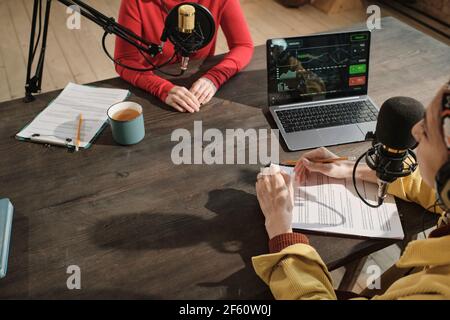 Frau sitzt am Tisch mit Dokument und Laptop und Befrachtend Gast während der Sendung im Radio Stockfoto