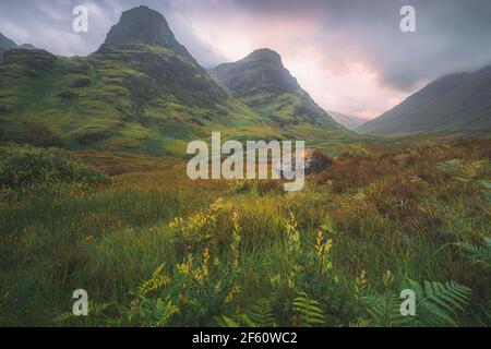 Moody, atmosphärische Berglandschaft der üppigen, grünen Three Sisters of Glencoe bei einem Sommer-Sonnenuntergang oder Sonnenaufgang in den Scottish Highlands, Scotlan Stockfoto