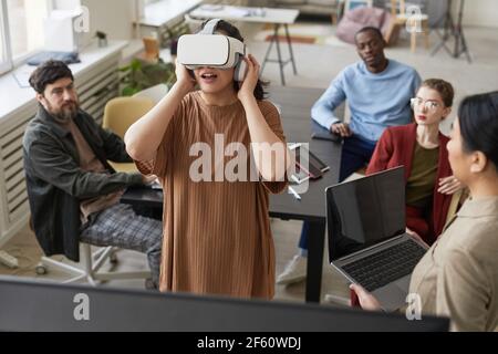 Vielfältiges IT-Entwicklungsteam, das an Virtual-Reality-Software im Büro arbeitet, konzentriert sich auf junge Frau, die VR-Headset im Vordergrund trägt Stockfoto