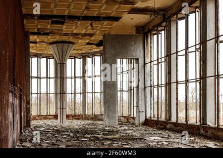 Der zerstörte Saal eines alten Gebäudes mit breiten Fenstern. Zerbrochenes Glas auf dem Boden. Stockfoto