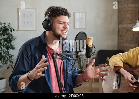 Junge männliche Sängerin in Kopfhörern singen ein Lied in Mikrofon Im Aufnahmestudio Stockfoto