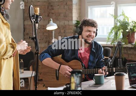 Reifer Mann in Kopfhörer spielen Gitarre im Radiostudio während Rundfunk Stockfoto