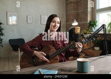 Portrait einer jungen Frau, die beim Gitarrenspiel lächelt Während der Funkübertragung Stockfoto