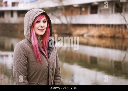 Durchbohrte junge Frau mit rosa Haaren und Kapuze Parka stehend Auf dem Fluss Stockfoto