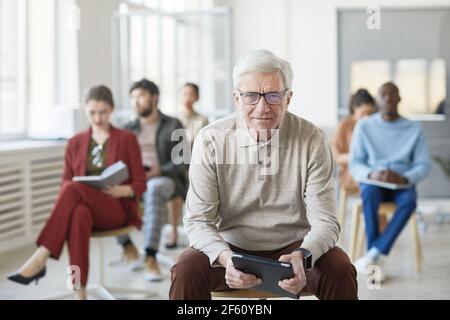 Verschiedene Gruppe von Geschäftsleuten sitzen auf Stühlen im Büro, konzentrieren sich auf moderne ältere Mann Blick auf Kamera Stockfoto