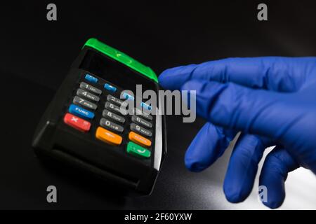 Hand in blauem Handschuh in der Nähe des elektronischen Terminals, auf schwarzem Hintergrund. Stockfoto