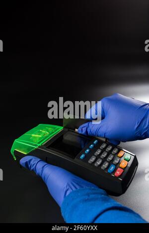 Hände in blauen Handschuhen, die eine Karte auf dem elektronischen Terminal auf schwarzem Hintergrund schieben. Stockfoto