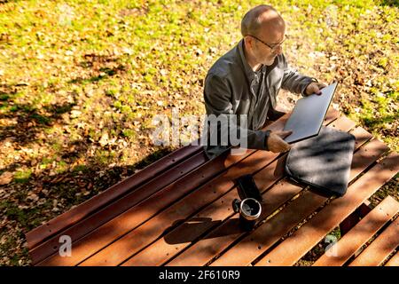 Mann, der sich aufsetzt, um im Park an einem Picknicktisch zu arbeiten Stockfoto