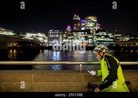 Radfahrer mit Telefon in der Stadt bei Nacht, London, Großbritannien Stockfoto