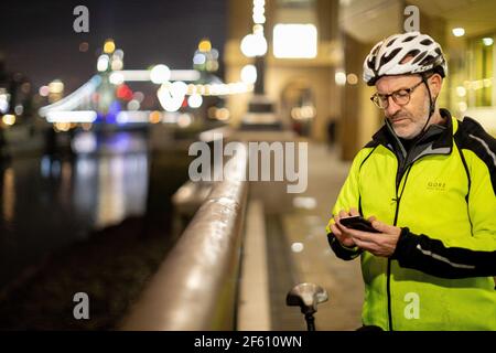 Fahrradfahrer, der nachts in der Stadt telefoniert, London, Großbritannien Stockfoto